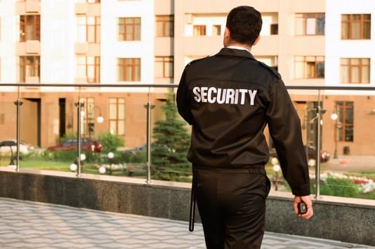 A security guard walking on the sidewalk near some buildings.