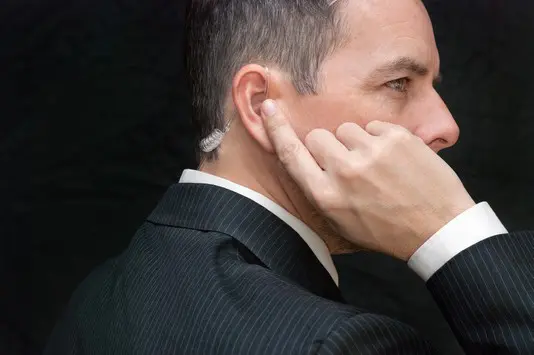 A man in a suit and tie holding his ear.