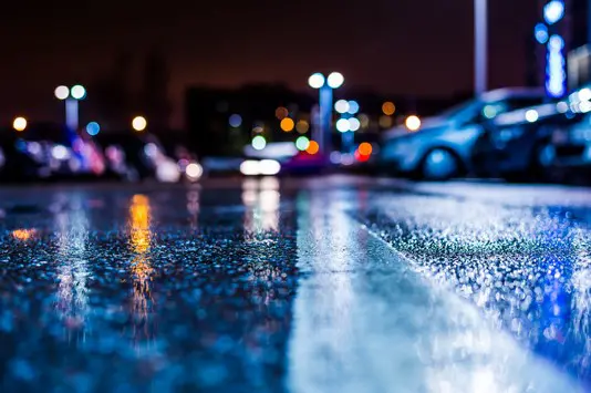 A wet road with lights on the side of it