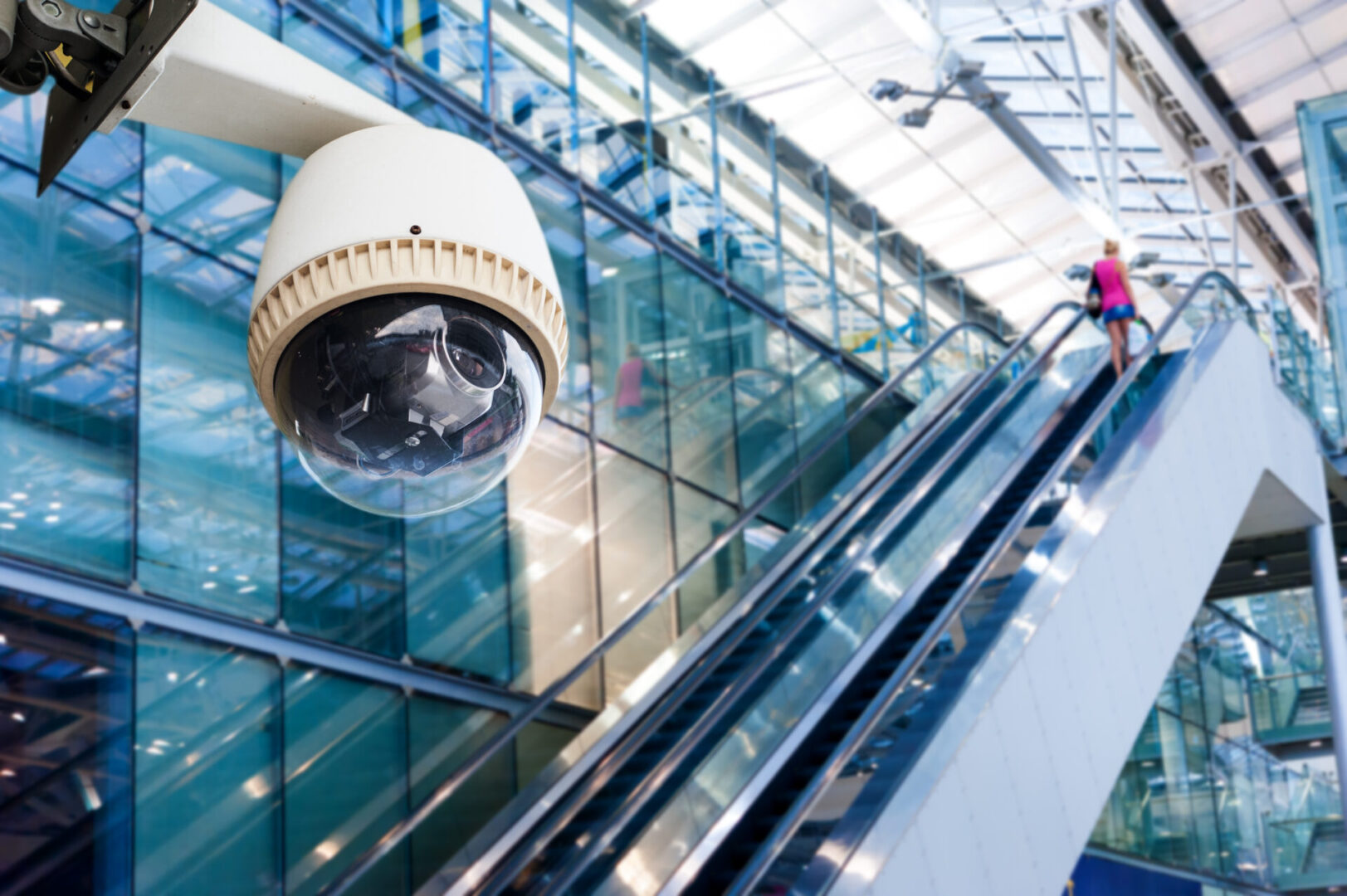 A security camera is mounted on the side of an escalator.