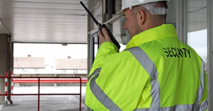 A security man reporting to HQ on a walkie talkie after checking the security of a entrance to a office block.